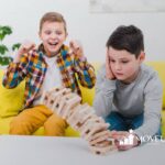 Two boys with autism react to a falling Jenga tower, one celebrating and the other upset.
