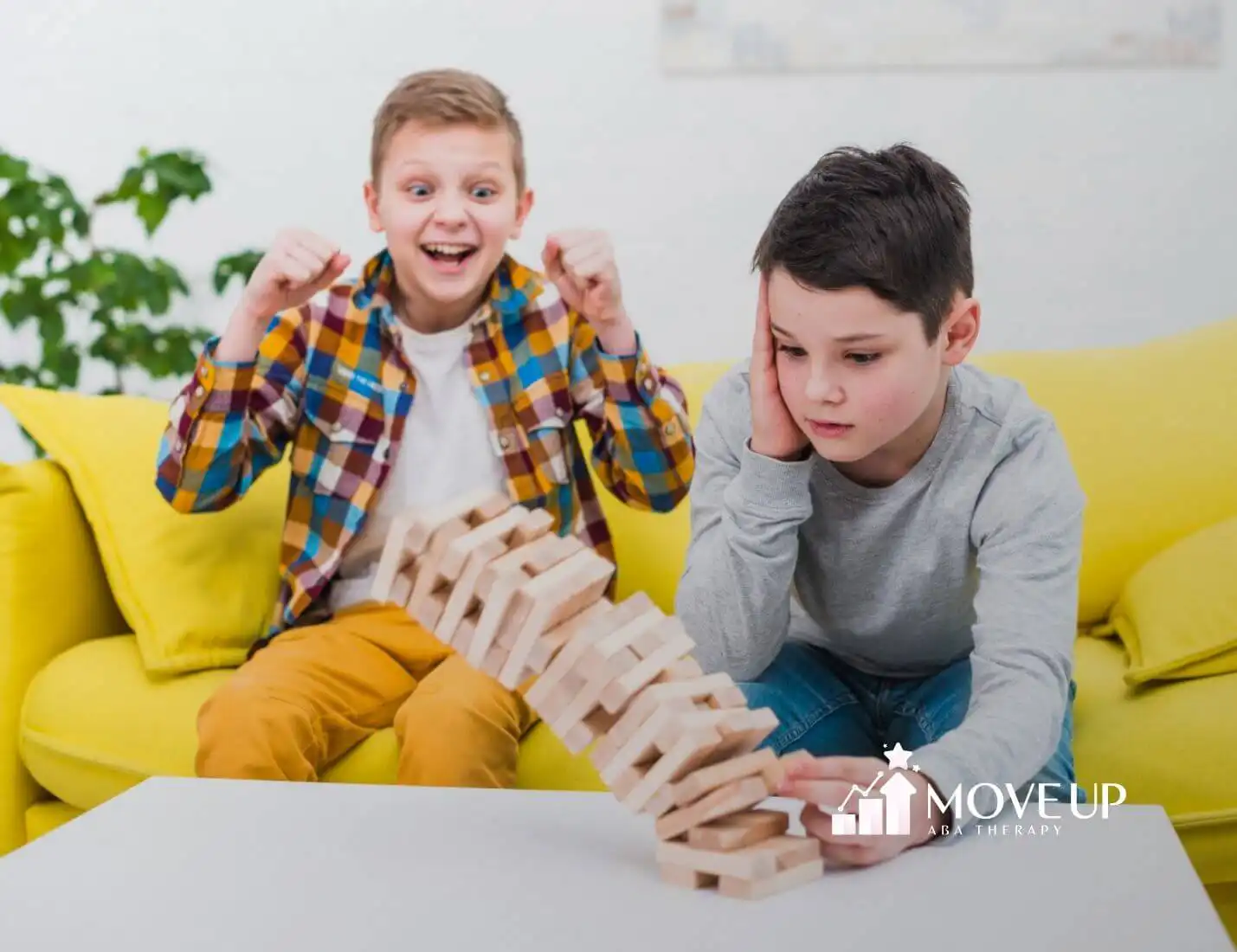 Two boys with autism react to a falling Jenga tower, one celebrating and the other upset.