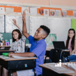 Autistic students sitting at desks in a classroom, raising hands to answer a question during school-based ABA therapy in MD.