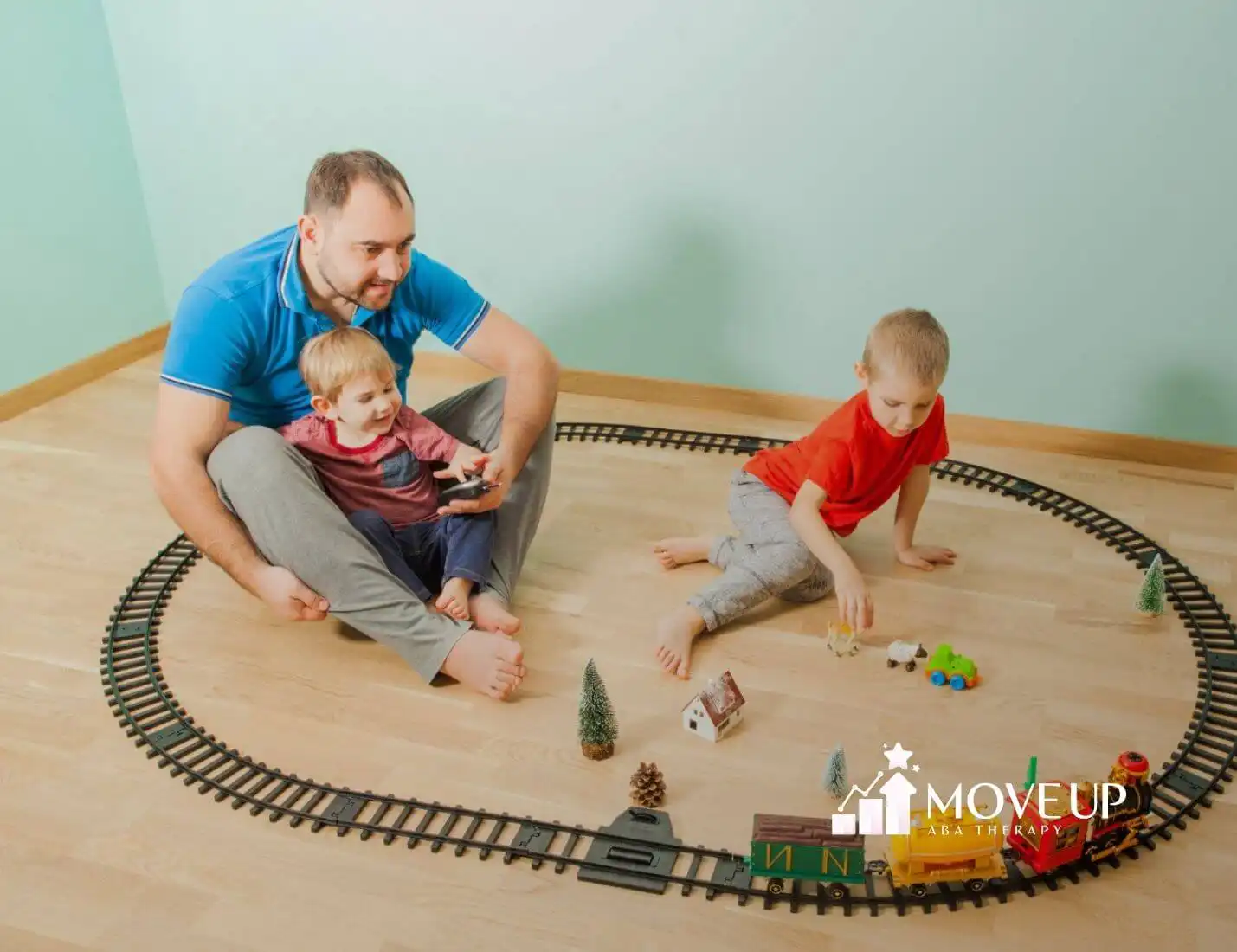 A father and two children play with a toy train set on the floor after in-home ABA therapy session.