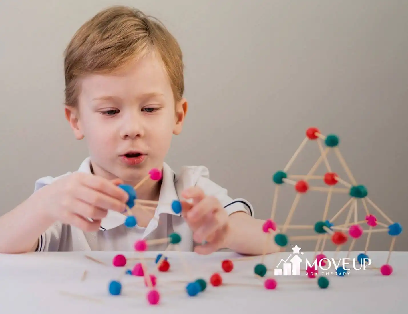 Autistic boy building a structure with sticks and colorful clay balls in ABA therapy.