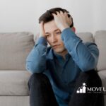 A man with autism sitting on the floor looking stressed and holding his head.
