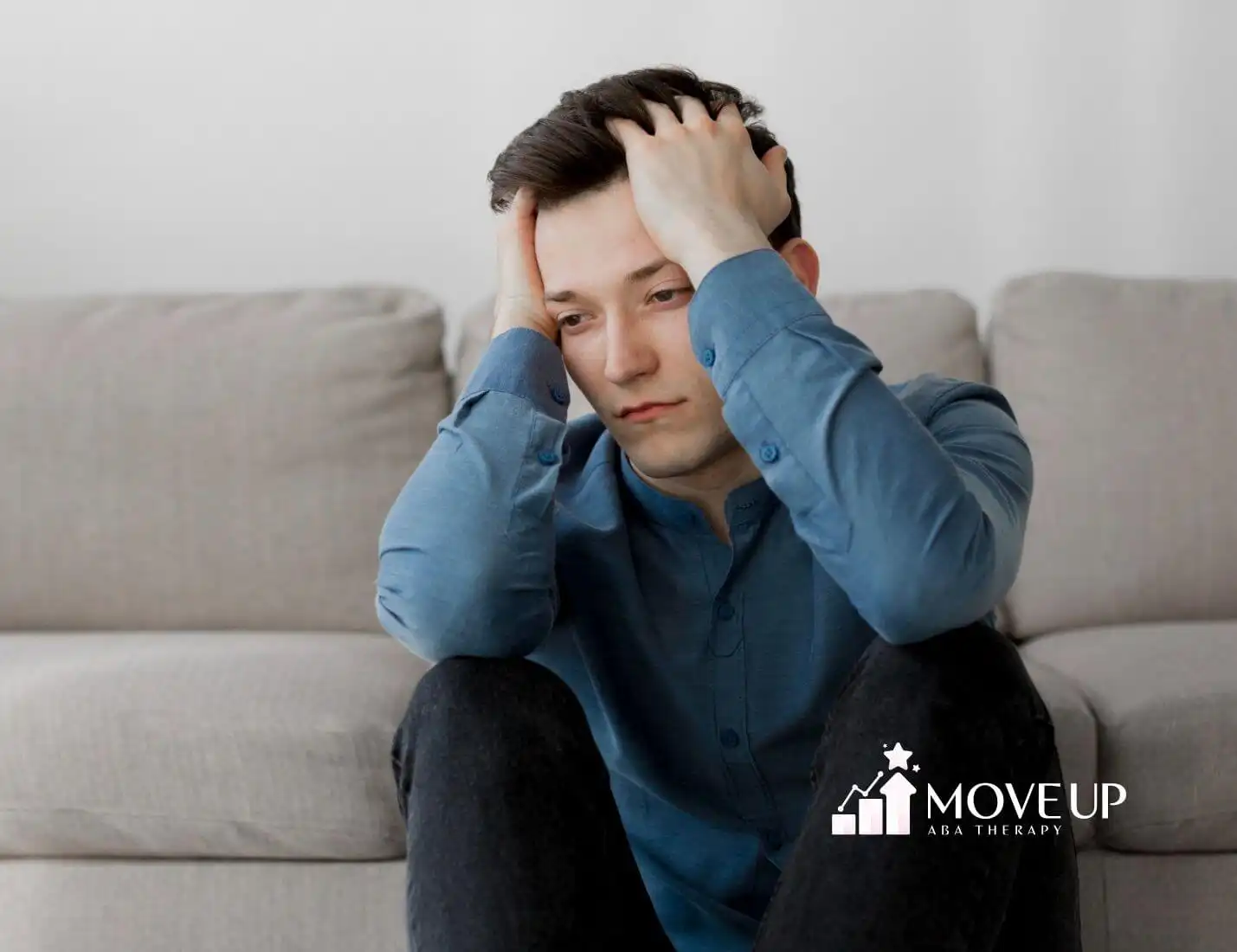 A man with autism sitting on the floor looking stressed and holding his head.