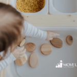 An autistic toddler pointing at smooth wooden sensory stones in a white sensory bin during ABA therapy session in Maryland.