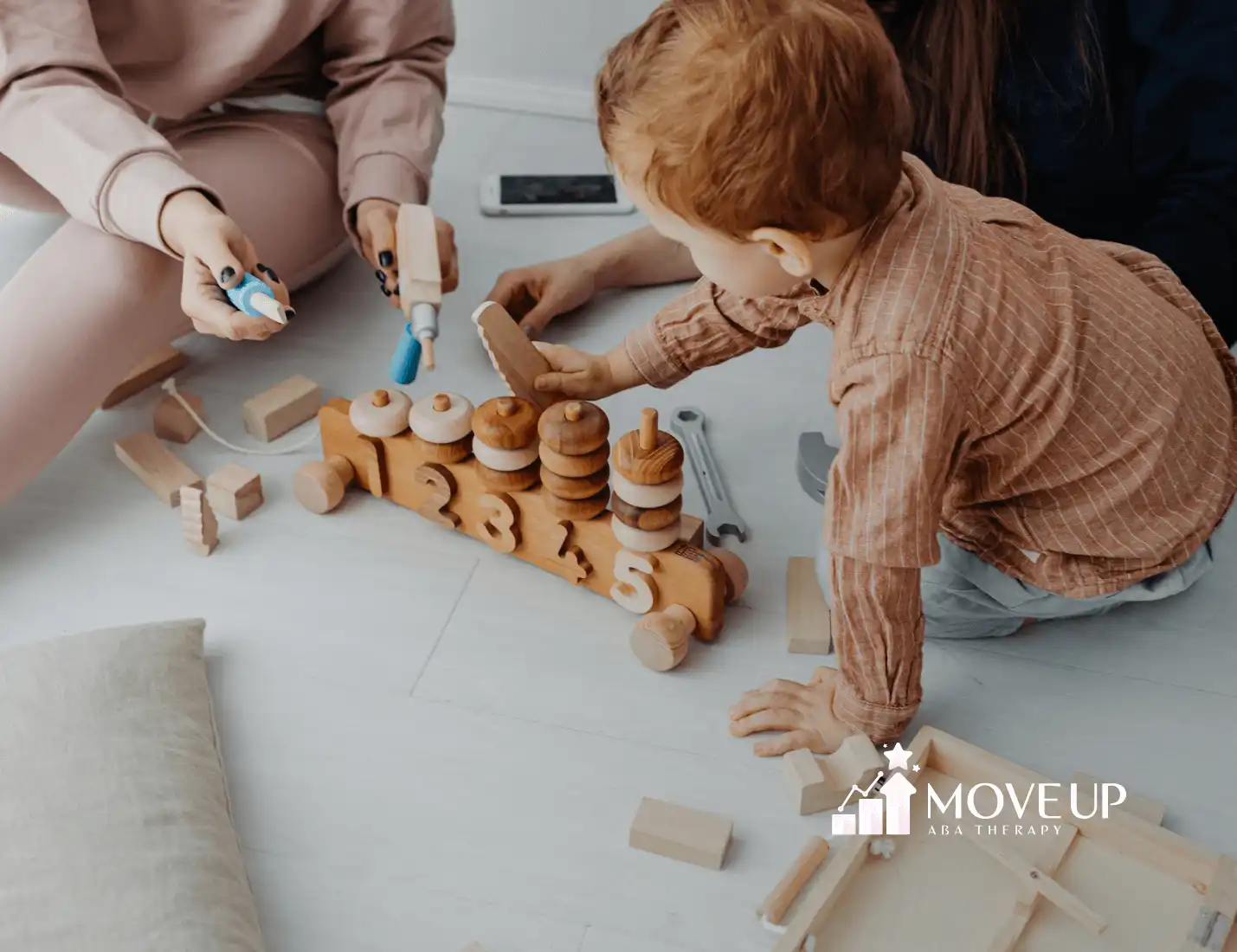 An autistic toddler playing with a wooden number toy and tools on the floor with adults during ABA therapy session in VA.