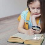 A girl with autism reading a book with a magnifying glass.