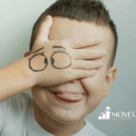 A kid making a silly face while covering his eyes with his hand with a drawing of silly eyes