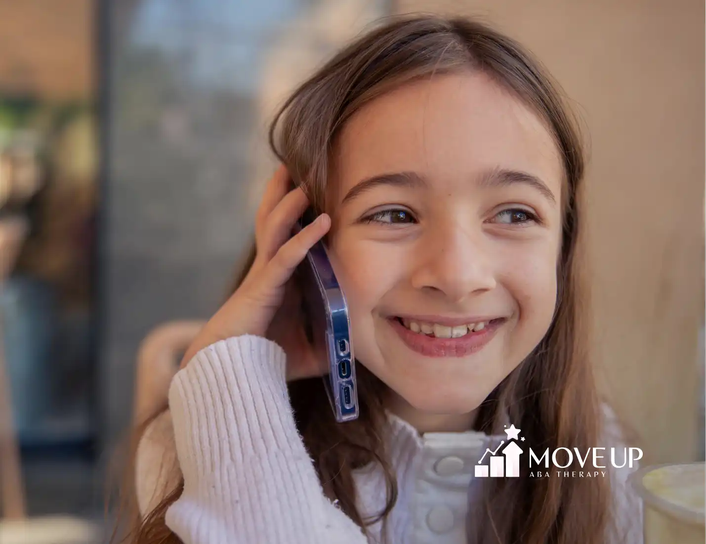 A child with autism is smiling while talking to someone over the phone