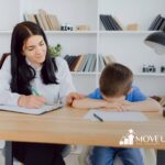 ABA therapist comforting autistic with head down at desk during ABA therapy session.
