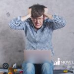 Frustrated man with autism pulling his hair while working on a laptop at a messy desk.