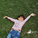 Smiling autistic child lying on grass with arms outstretched during school-based ABA therapy in Virginia.