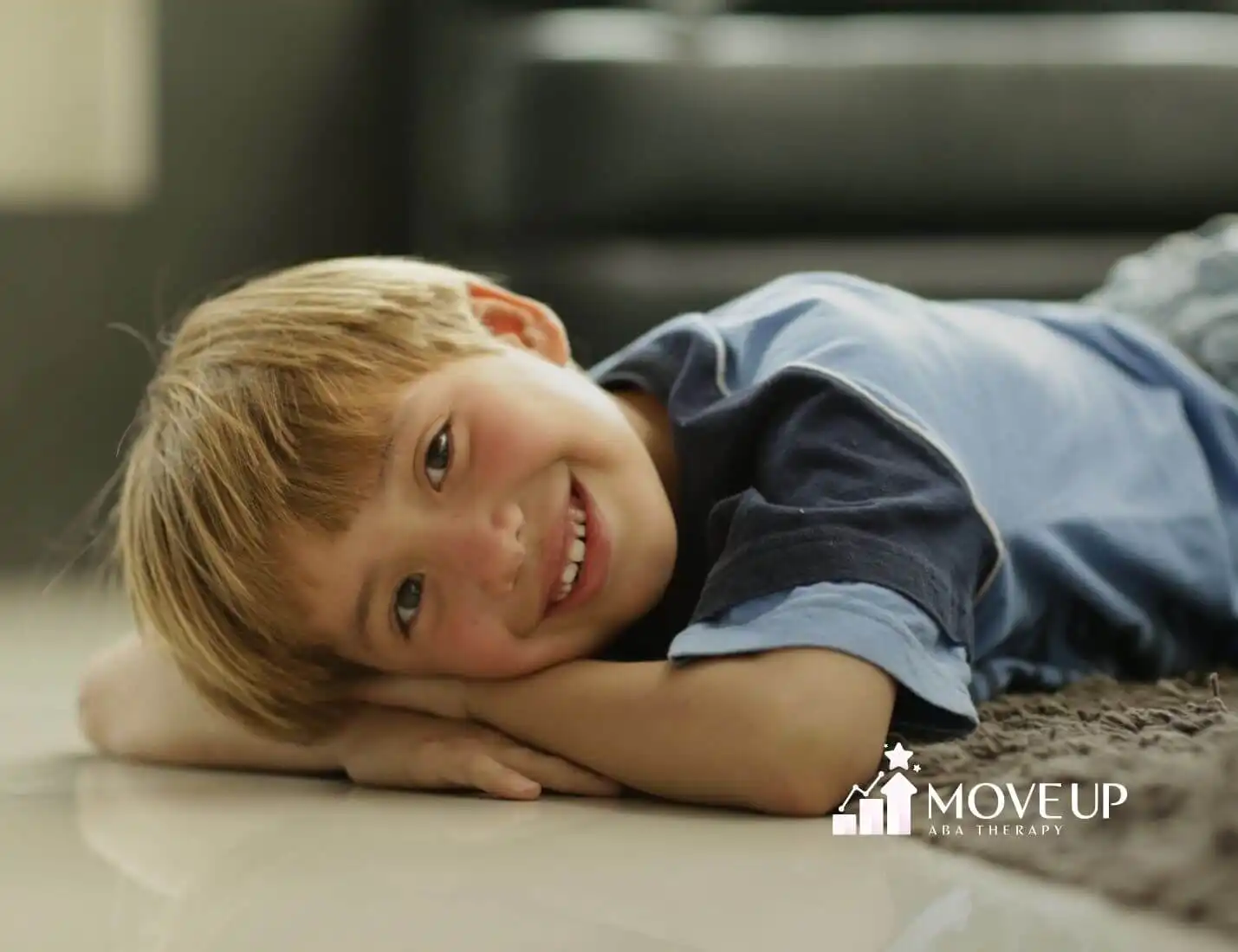 Boy with autism lying on the floor smiling at the camera.