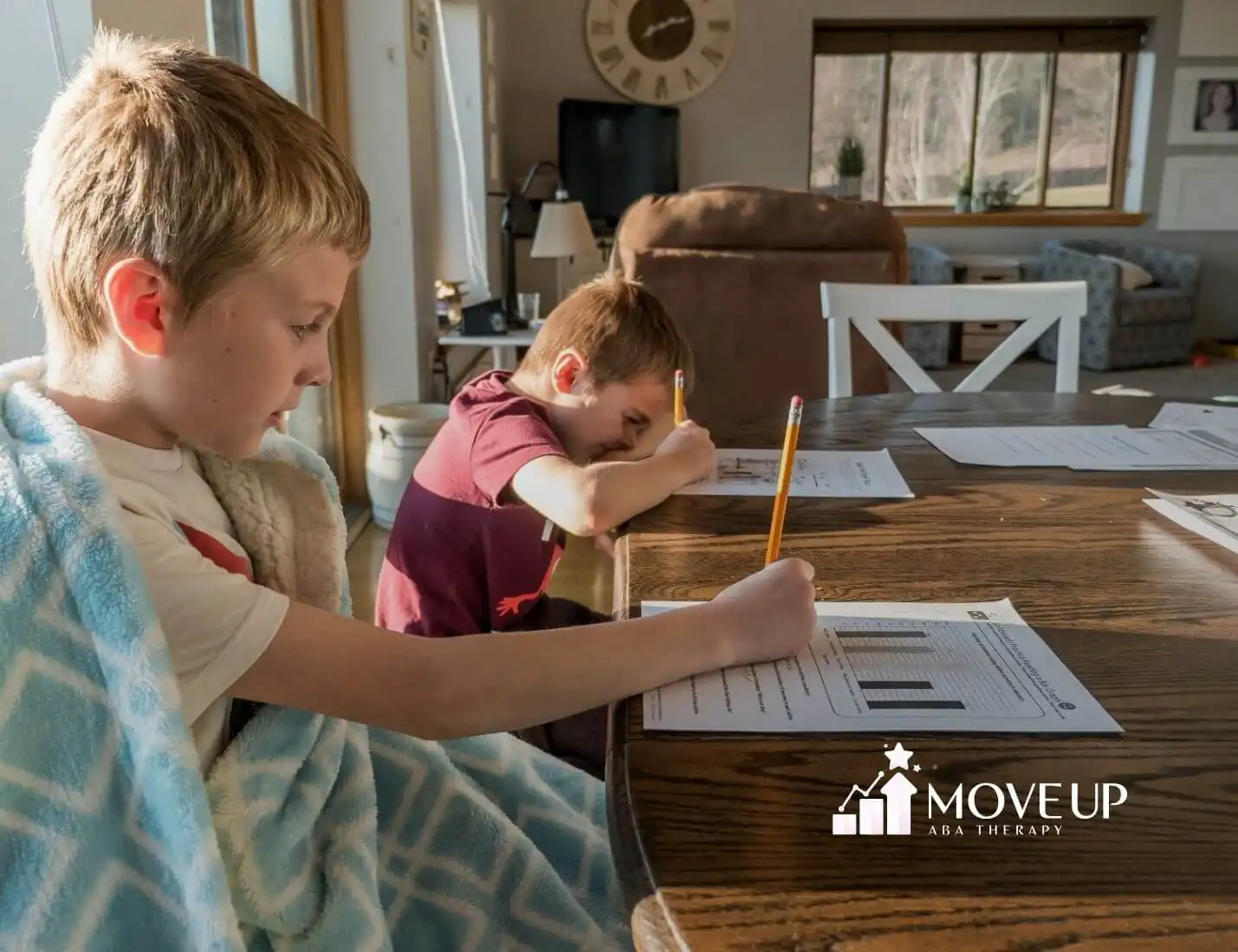 Two autistic young boys sitting at a table working on homework with pencils and worksheets after ABA therapy.