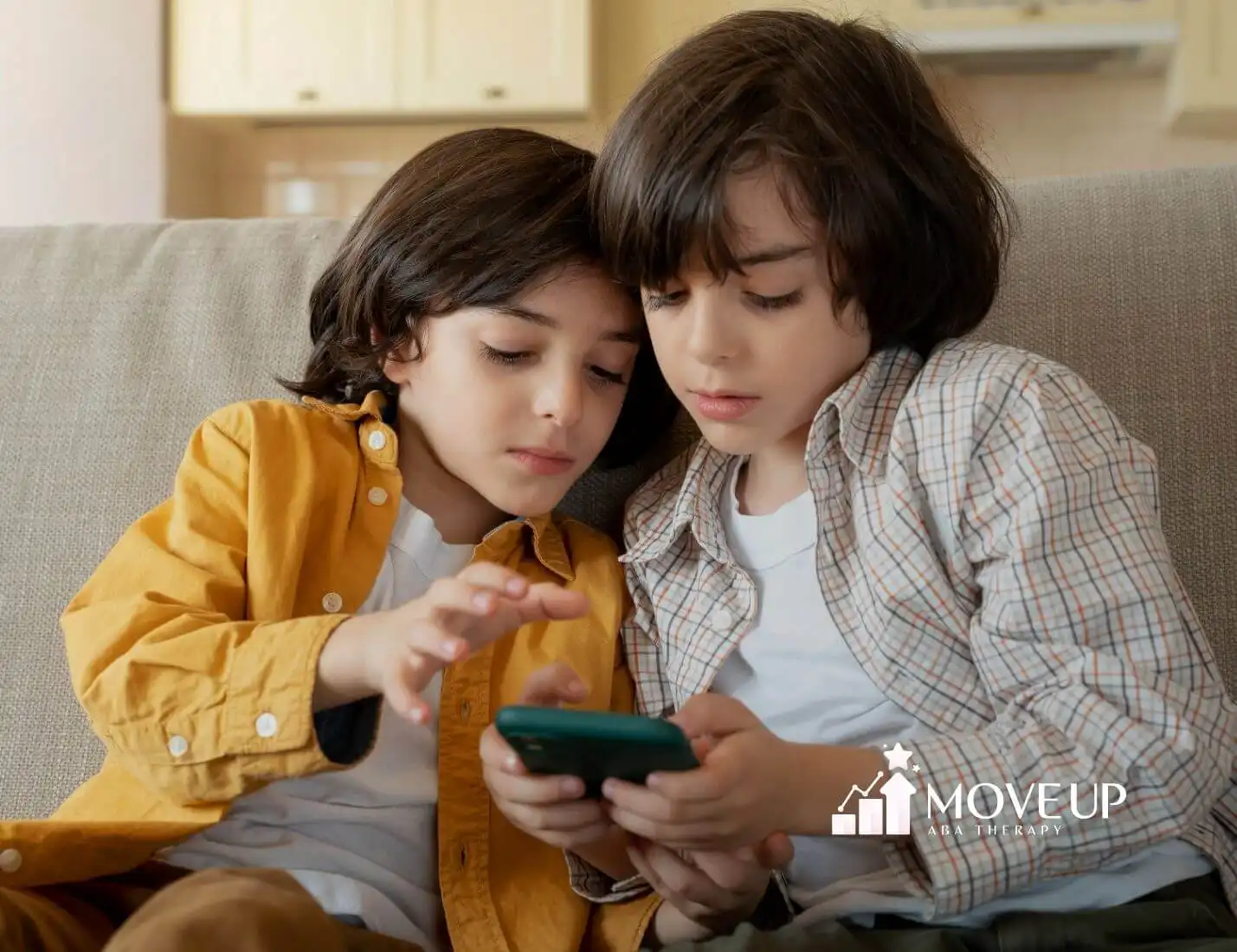 Two autistic boys sitting closely together on a couch, focused on a smartphone screen while interacting.