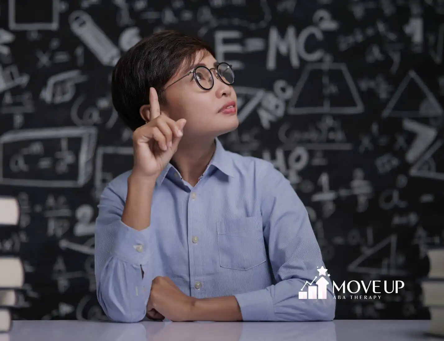 ABA therapist with glasses sitting at a desk, raising his finger as if coming up with a solution, surrounded by math symbols.