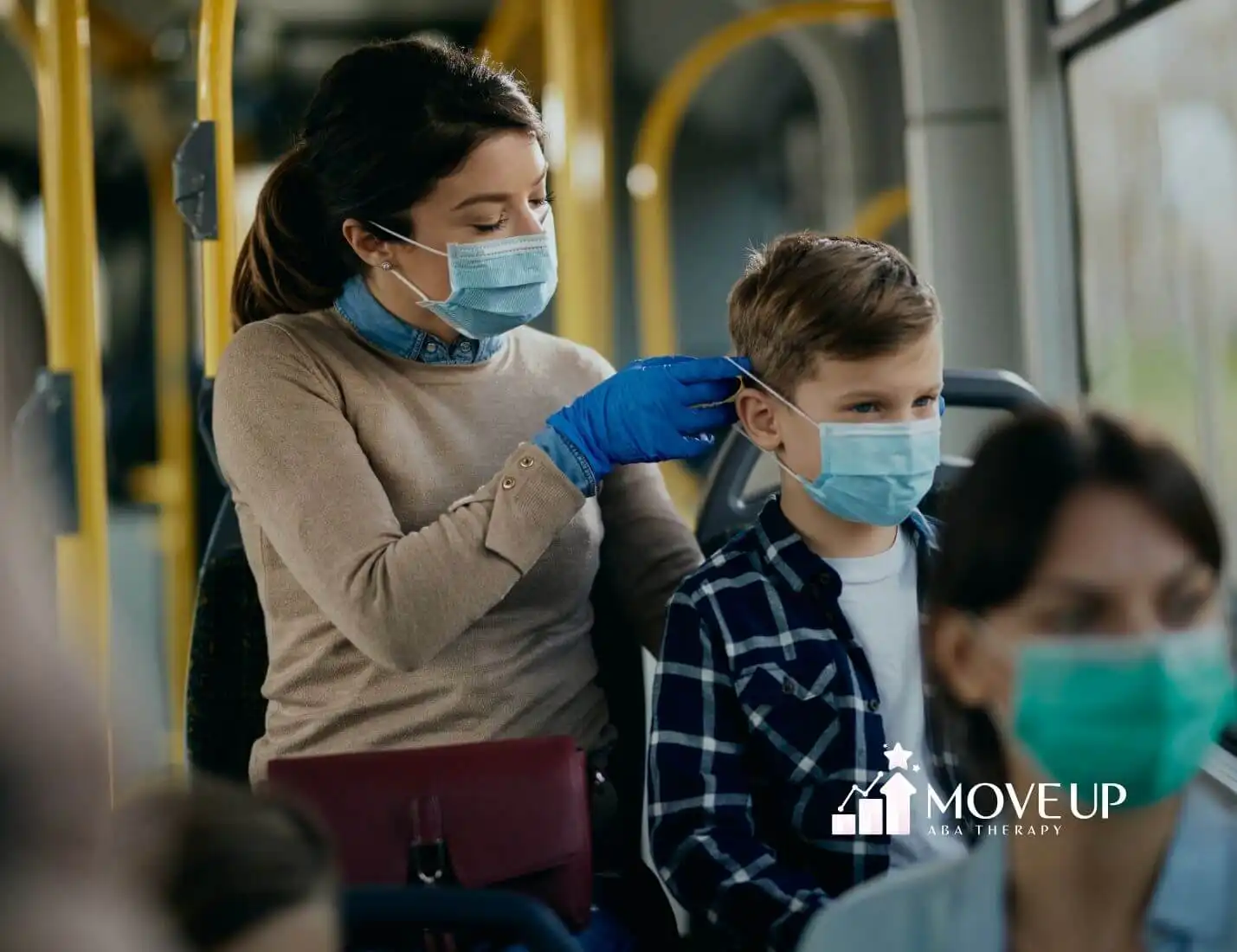 ABA therapist wearing a mask putting a mask on her young autistic son on a bus, both smiling while others sit nearby.