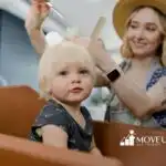 Autistic toddler with blonde hair getting a haircut from a smiling hairdresser.