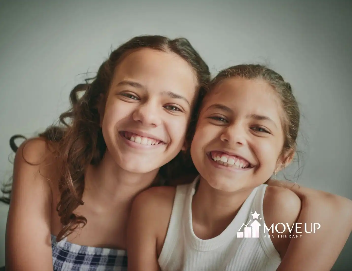 Two young girls smiling warmly, conveying joy and friendship. The background is plain, focusing on their expressions.