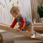 Smiling toddler in a striped shirt climbs a wooden ramp in a bright, plant-themed playroom