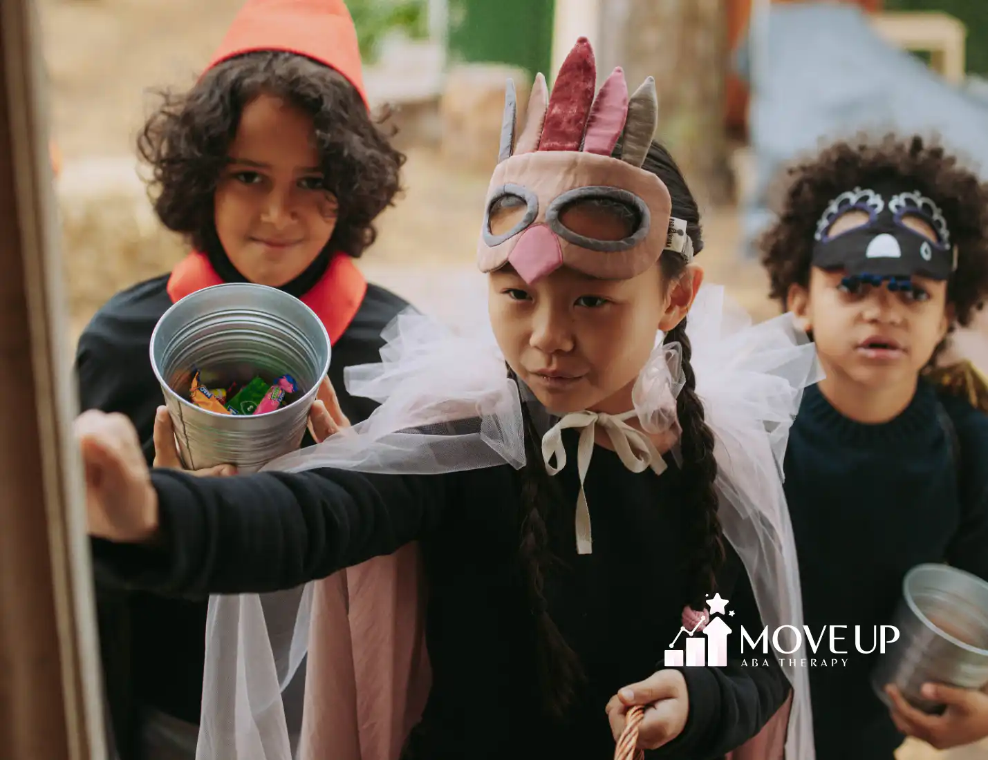 Three children in Halloween costumes and masks holding metal buckets of candy at a doorway