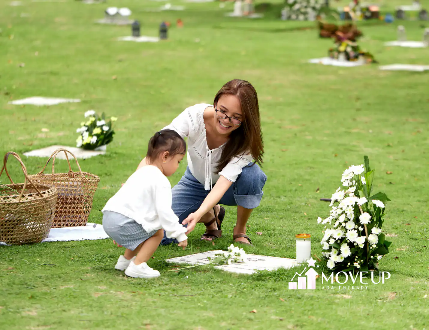 Woman kneeling on grass with a young child placing white flowers on a flat memorial marker