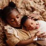 Young girl lying on a soft blanket holding her sleeping swaddled newborn sibling